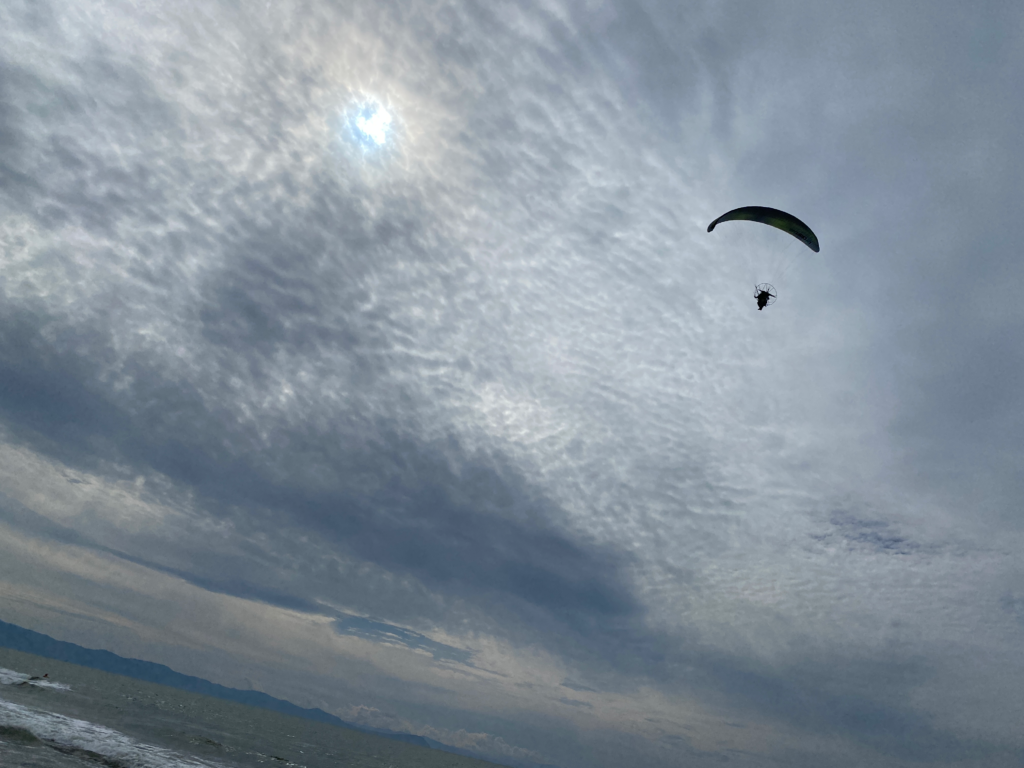 広がる雲の下を飛ぶパラグライダー